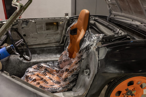Custom orange racing seat installed in a 1963 Corvette Sting Ray, wrapped for protection during build