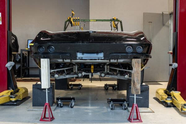 Bare 1963 Corvette Sting Ray body in black primer, hoisted onto stands for restoration at Crown Customs