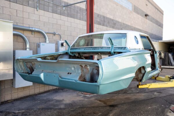 1966 Ford Thunderbird body shell in its original mint paint, hoisted for a full frame-off restoration at Crown Customs