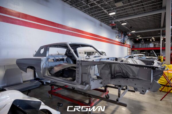 Side profile of a 1966 Ford Thunderbird shell in primer on a rotisserie at Crown Customs