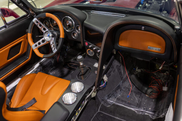 Finished interior of a 1963 Corvette Sting Ray restomod with orange and black seats and digital gauges