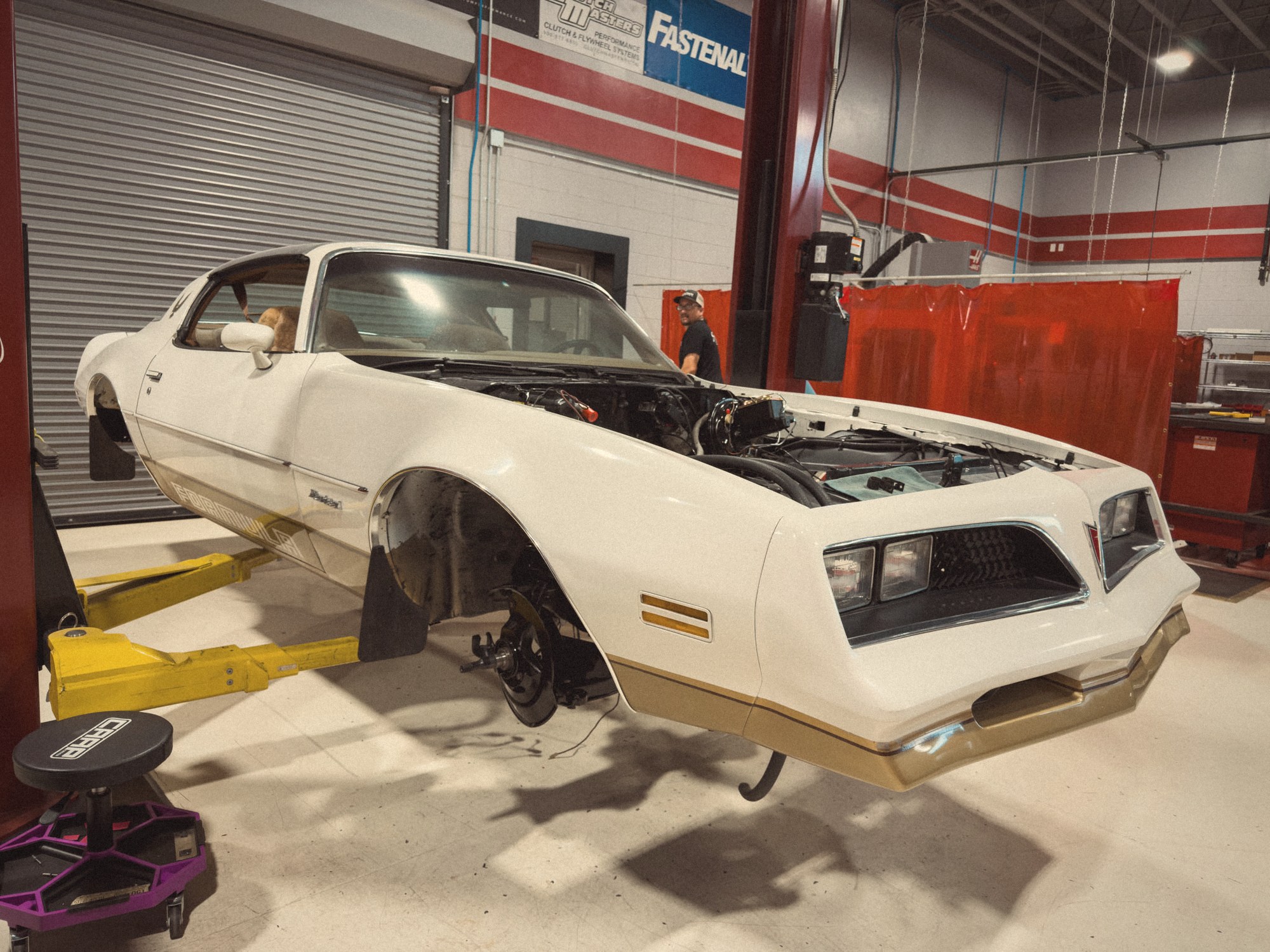 The white and gold 1978 Pontiac Firebird Formula on the lift at Crown Customs, finished in a warm period tone that recalls a 1970s Pontiac brochure