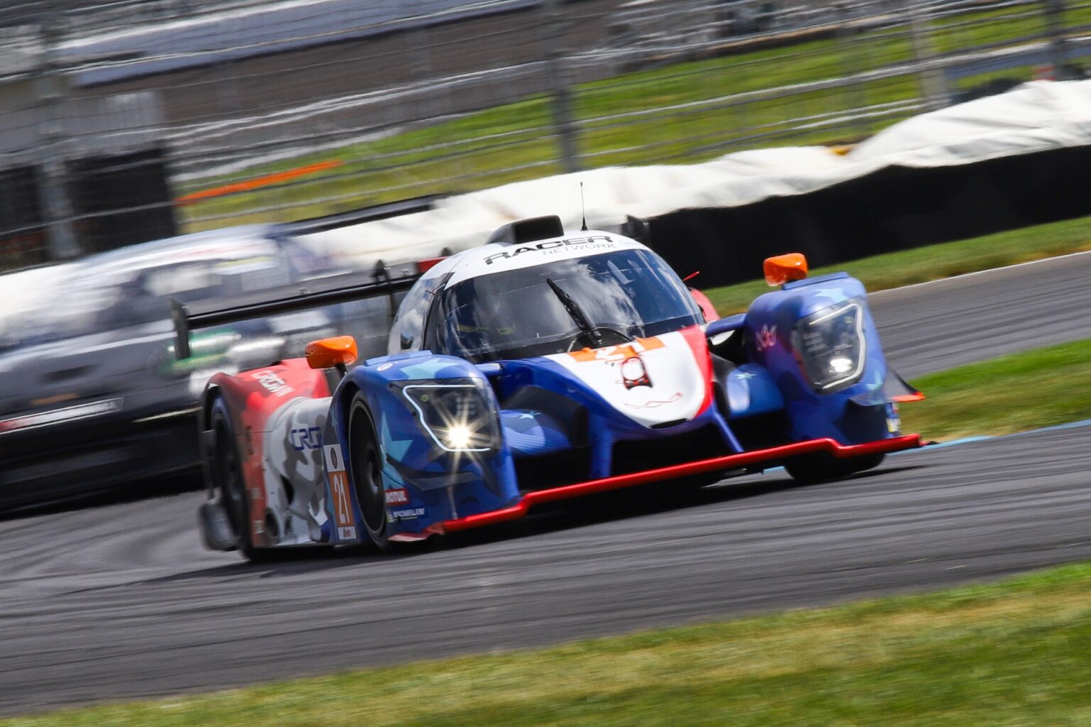 Crown Racing prototype at speed on the road course at Indianapolis Motor Speedway with the grandstands behind