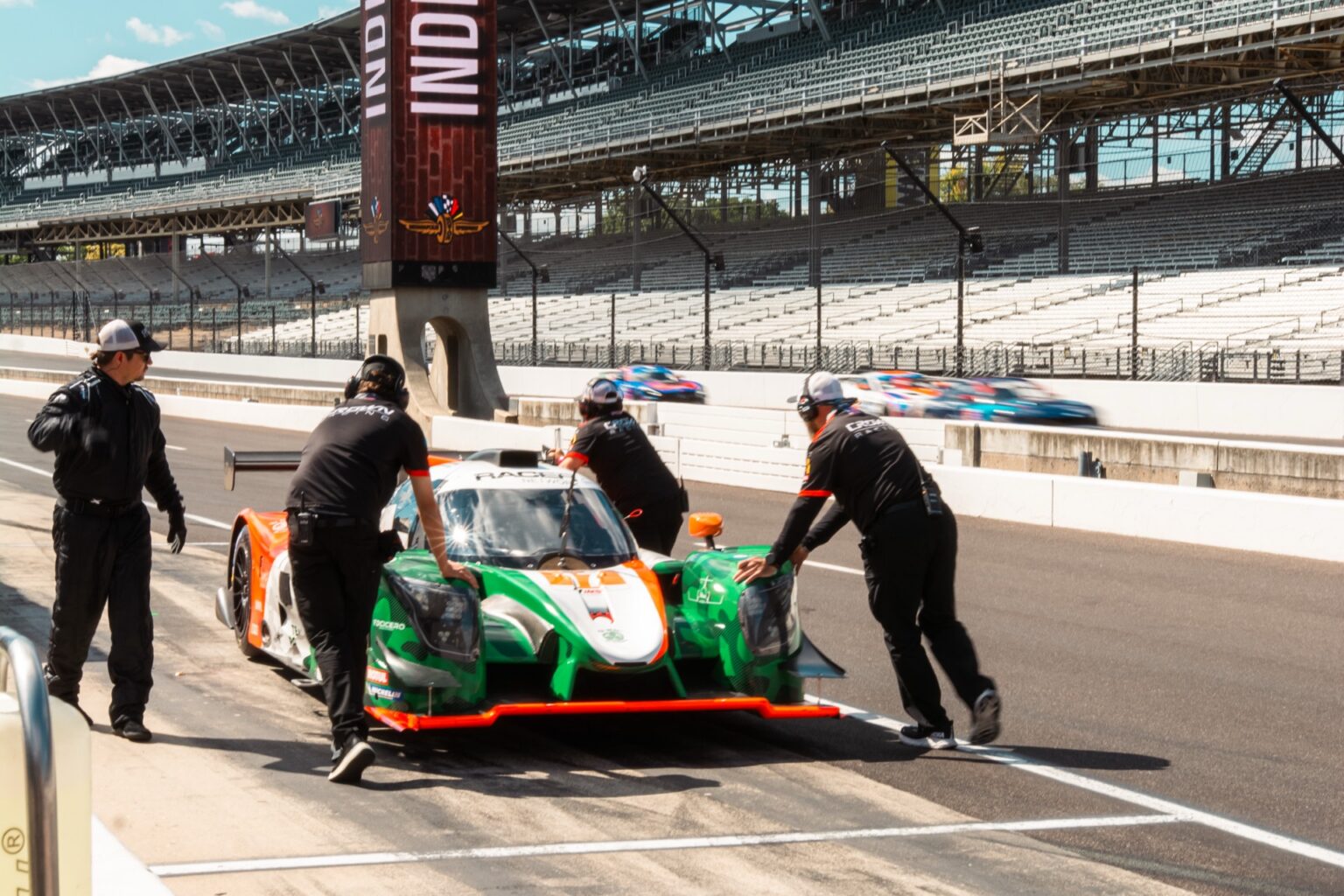 Crown Racing prototypes on pit lane at Indianapolis Motor Speedway with the main grandstand and Indy banners behind them