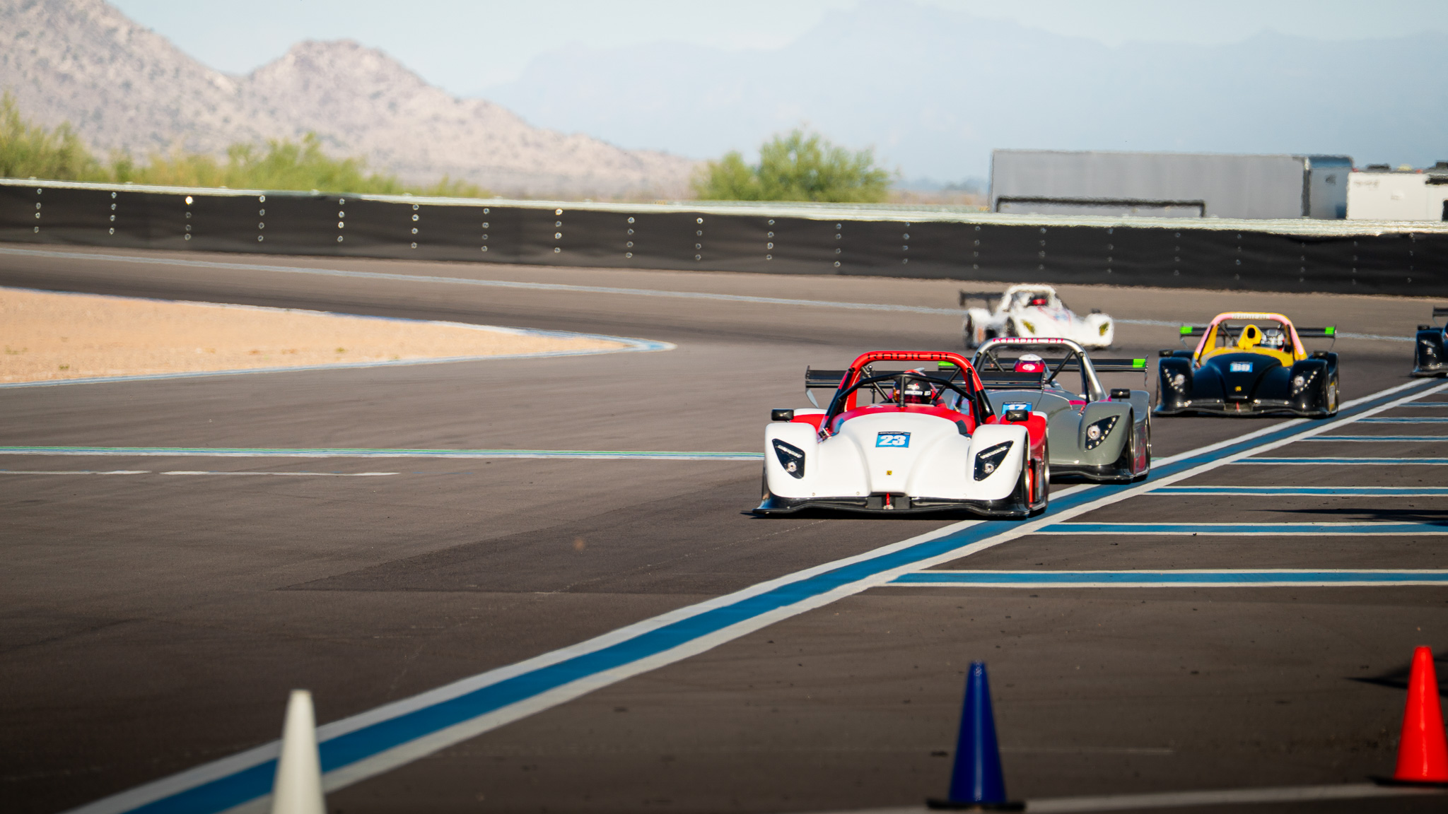 A group of Radical prototypes racing toward the camera at Apex Motor Club with desert mountains behind