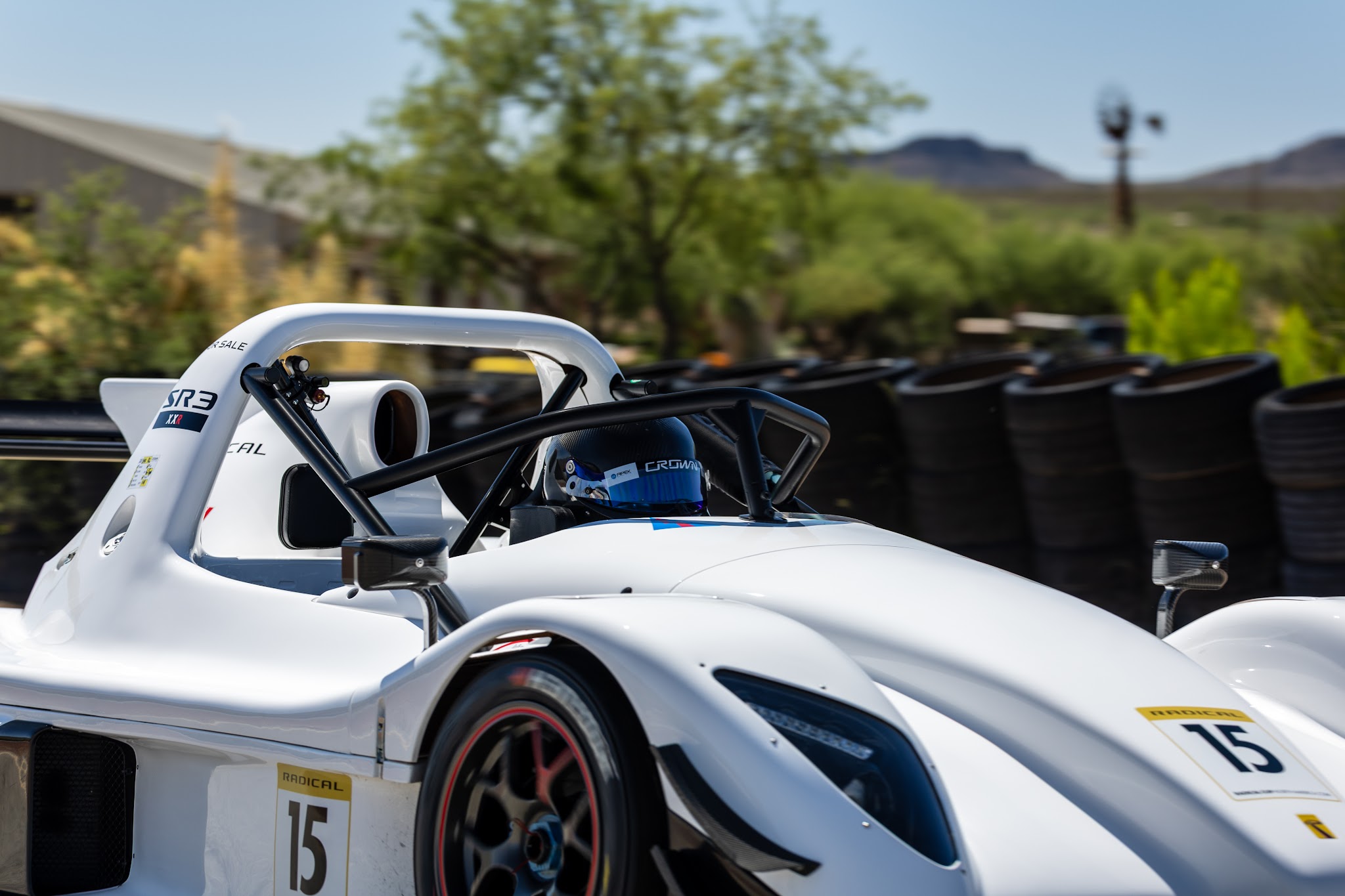 Ryan George seated in his white number 15 Radical SR3 XXR beside the tire wall at Inde Motorsports Ranch