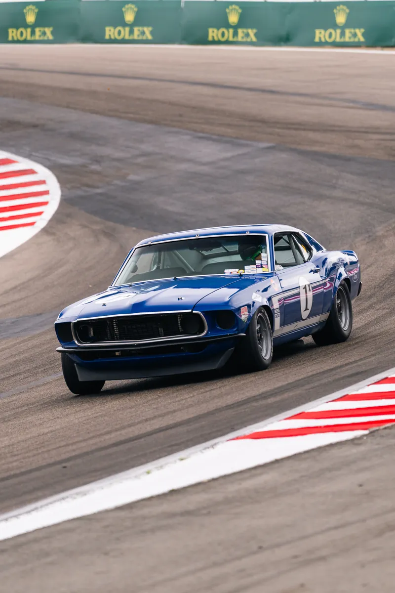 Blue No. 1 Mustang race car cornering at Laguna Seca with Rolex banners behind